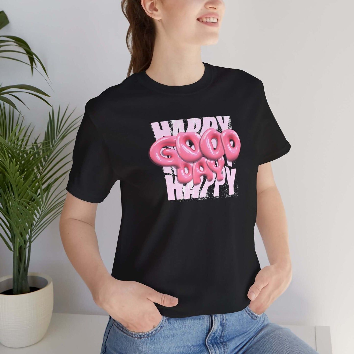 Woman wearing a playful Happy Good Vibes graphic tee, ideal for casual wear and parties, surrounded by indoor plants.