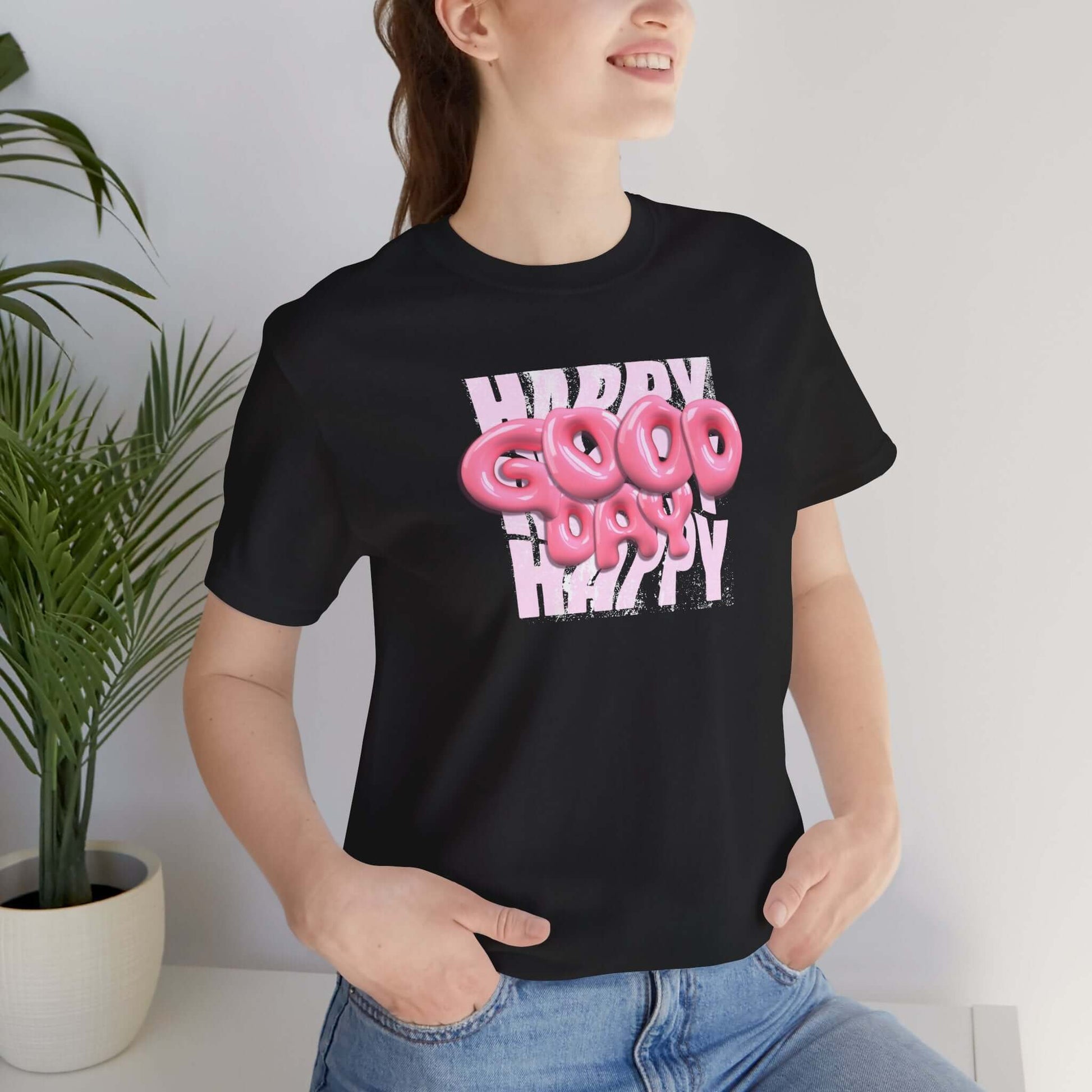 Woman wearing a playful Happy Good Vibes graphic tee, ideal for casual wear and parties, surrounded by indoor plants.